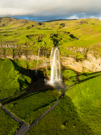 Aerial view of Seljalandsfoss waterfall cascading over a dramatic cliff surrounded by lush green meadows and walking paths Rangarthing eystra Iceland. Aerial view of Seljalandsfoss waterfall cascading over a dramatic cliff surrounded by lush green meadows and walking paths Rangarthing eystra Iceland.