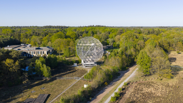 Aerial view of the Dwingeloo Radio Observatory dish surrounded by lush green forest and research buildings under a clear blue sky in Dwingeloo Drenthe Netherlands.
