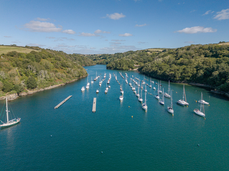 Aerial view of numerous sailboats and yachts moored in the Fowey river surrounded by lush green hills and the coastal landscape of Fowey Cornwall United Kingdom. Aerial view of numerous sailboats and yachts moored in the Fowey river surrounded by lush green hills and the coastal landscape of Fowey Cornwall United Kingdom.