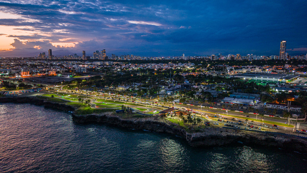 Aerial view of Feria Ganadera park along the coastline at dusk featuring illuminated roads palm trees and the city skyline in the background Santo Domingo Distrito Nacional Dominican Republic. Aerial view of Feria Ganadera park along the coastline at dusk featuring illuminated roads palm trees and the city skyline in the background Santo Domingo Distrito Nacional Dominican Republic.