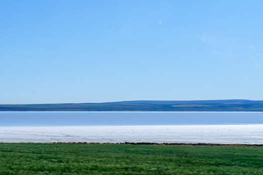 View of the white salt flats of Lake Tuz with green fields in the foreground and a clear blue sky Ankara Ankara Turkiye.