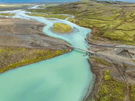 Aerial view of the turquoise glacial river flowing through the rugged mossy landscape of Kerlingarfjoll with a bridge crossing the water in Hrunamannahreppur Iceland. Aerial view of the turquoise glacial river flowing through the rugged mossy landscape of Kerlingarfjoll with a bridge crossing the water in Hrunamannahreppur Iceland.