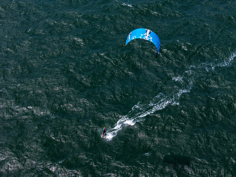 Aerial view of a kitesurfer gliding across the dark choppy waters of Depok Beach in the Special Region of Yogyakarta Indonesia. Aerial view of a kitesurfer gliding across the dark choppy waters of Depok Beach in the Special Region of Yogyakarta Indonesia.