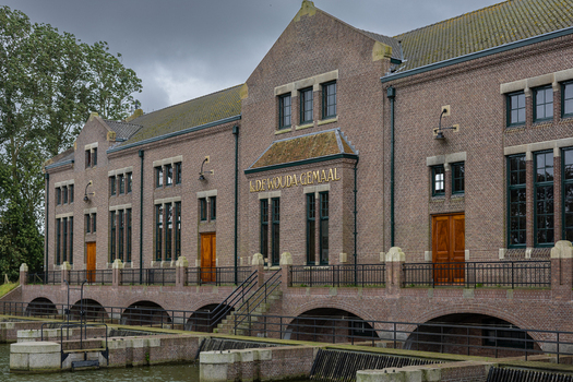 View of the historic Wouda pumping station with its impressive brick facade and arched foundations over the water canal under a cloudy sky in Lemmer Friesland Netherlands.