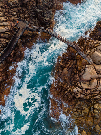 Aerial view of the wooden Canal Rocks Bridge spanning rugged granite formations with crashing turquoise waves and white sea foam in Yallingup Western Australia Australia. Aerial view of the wooden Canal Rocks Bridge spanning rugged granite formations with crashing turquoise waves and white sea foam in Yallingup Western Australia Australia.
