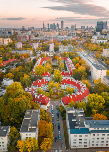 Aerial view of residential buildings with bright red roofs surrounded by autumn trees and the modern city skyline under a soft sunset sky in Poland. Aerial view of residential buildings with bright red roofs surrounded by autumn trees and the modern city skyline under a soft sunset sky in Poland.
