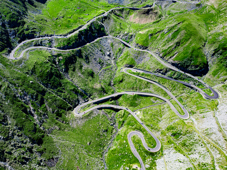 Aerial view of the winding Transfagarasan mountain road with its sharp hairpin turns and steep slopes surrounded by lush green mountains in Curtea de Arges Judetul Arges Romania. Aerial view of the winding Transfagarasan mountain road with its sharp hairpin turns and steep slopes surrounded by lush green mountains in Curtea de Arges Judetul Arges Romania.
