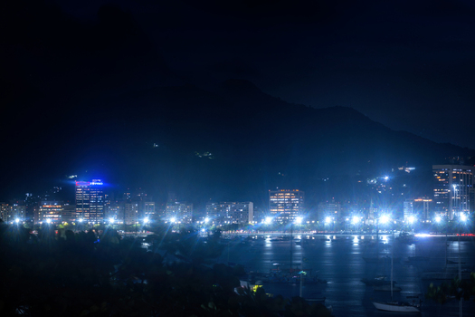 View of the illuminated skyline and Botafogo bay with boats anchored in the water under dark mountains in Rio de Janeiro State of Rio de Janeiro Brazil. View of the illuminated skyline and Botafogo bay with boats anchored in the water under dark mountains in Rio de Janeiro State of Rio de Janeiro Brazil.