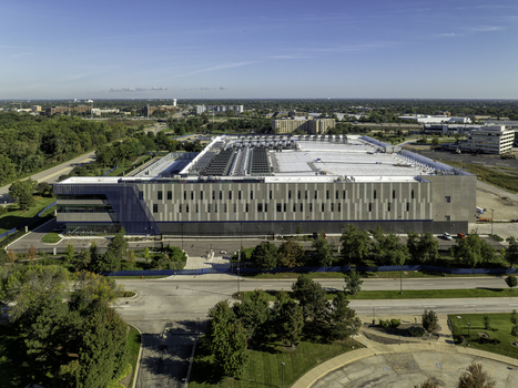 Aerial view of a large modern data center facility with a flat roof and cooling units surrounded by green trees and roads in Elk Grove Village Illinois United States.