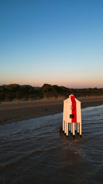 Aerial view of the Burnham on Sea Low Lighthouse standing on stilts on the sandy beach at sunset with calm waves and a clear sky in Burnham on Sea England United Kingdom. Aerial view of the Burnham on Sea Low Lighthouse standing on stilts on the sandy beach at sunset with calm waves and a clear sky in Burnham on Sea England United Kingdom.