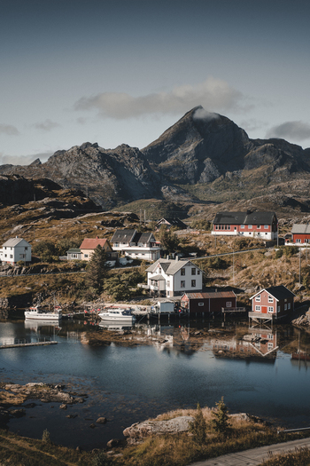 Sund Nordland Norway 08 September 2022 View of the coastal village of Sund with traditional red and white houses fishing boats in the harbor and dramatic rocky mountains.