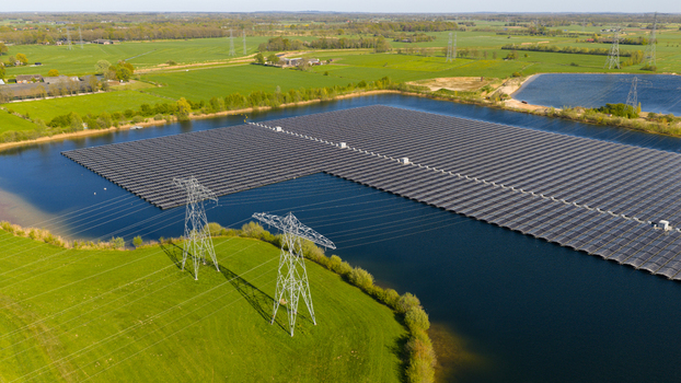 Aerial view of a floating solar panel farm on a lake surrounded by green fields and power pylons in Zwolle Overijssel Netherlands. Aerial view of a floating solar panel farm on a lake surrounded by green fields and power pylons in Zwolle Overijssel Netherlands.