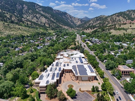 Aerial view of a large building complex with solar panels on the roof surrounded by lush green trees and the foothills of the Rocky Mountains in Boulder Colorado United States. Aerial view of a large building complex with solar panels on the roof surrounded by lush green trees and the foothills of the Rocky Mountains in Boulder Colorado United States.