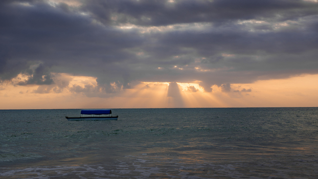 View of the sun s rays pierce through the dark dramatic clouds illuminating the tranquil turquoise ocean and a small boat Paje Tanzania. View of the sun s rays pierce through the dark dramatic clouds illuminating the tranquil turquoise ocean and a small boat Paje Tanzania.