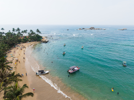 Aerial view of the sandy beach and turquoise ocean with boats and people along the coastline in Hikkaduwa Southern Province Sri Lanka. Aerial view of the sandy beach and turquoise ocean with boats and people along the coastline in Hikkaduwa Southern Province Sri Lanka.