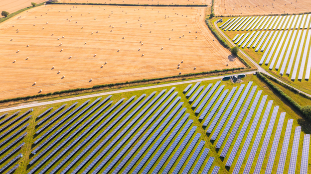 Aerial view of a large solar farm with rows of photovoltaic panels adjacent to a harvested field with hay bales in Dorset England United Kingdom. Aerial view of a large solar farm with rows of photovoltaic panels adjacent to a harvested field with hay bales in Dorset England United Kingdom.