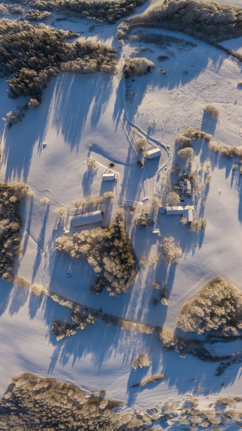 Aerial view of a snow covered rural landscape featuring scattered farm buildings frost covered trees and long shadows cast by the low winter sun in Latvia. Aerial view of a snow covered rural landscape featuring scattered farm buildings frost covered trees and long shadows cast by the low winter sun in Latvia.