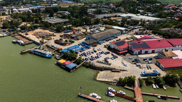 Aerial view of the industrial port area in Tulcea featuring warehouses with red roofs a parking lot and boats docked along the Danube riverbank in Tulcea Tulcea Romania. Aerial view of the industrial port area in Tulcea featuring warehouses with red roofs a parking lot and boats docked along the Danube riverbank in Tulcea Tulcea Romania.