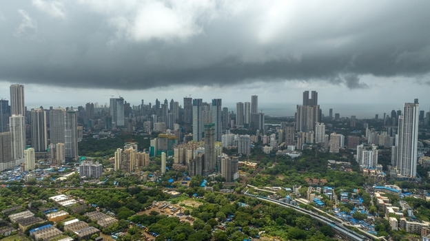 Aerial view of the dense Mumbai skyline featuring numerous skyscrapers modern high rise buildings and lush green areas under a dramatic overcast sky in Mumbai Maharashtra India.