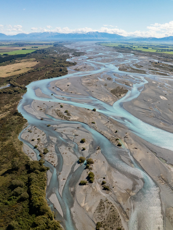 Aerial view of a braided river system snaking through the landscape carving paths amidst gravel beds under a vast sky Canterbury Region New Zealand. Aerial view of a braided river system snaking through the landscape carving paths amidst gravel beds under a vast sky Canterbury Region New Zealand.