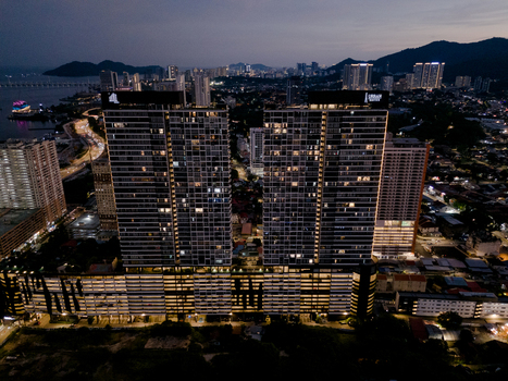 George Town Malaysia 12 April 2026 Aerial view of the Urban Suites high rise residential complex at twilight featuring illuminated windows city lights and distant hills.