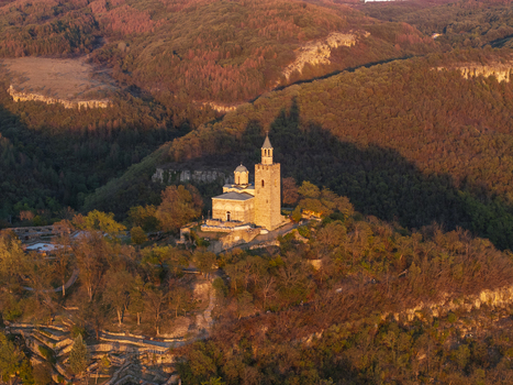 Aerial view of Tsarevets Fortress illuminated by golden hour light surrounded by lush forested hills and historic stone walls in Veliko Tarnovo Veliko Tarnovo Bulgaria. Aerial view of Tsarevets Fortress illuminated by golden hour light surrounded by lush forested hills and historic stone walls in Veliko Tarnovo Veliko Tarnovo Bulgaria.