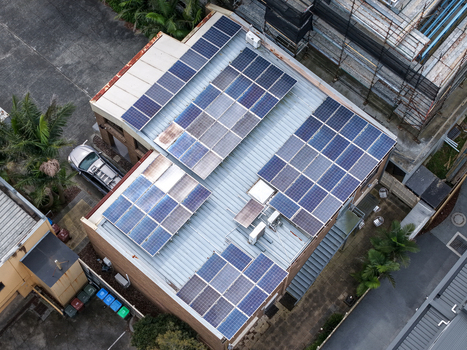 Melbourne Australia 25 September 2026 Aerial view of a building roof covered with solar panels featuring metal roofing palm trees and a parked vehicle.