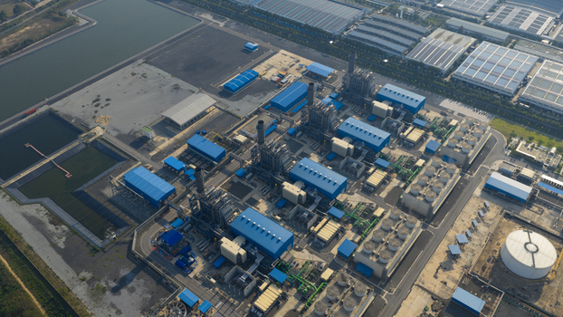 Aerial view of the Gulf Pluak Daeng Power Plant featuring industrial buildings with blue roofs tall smokestacks and cooling towers under clear sunlight in Map Yang Phon Rayong Thailand. Aerial view of the Gulf Pluak Daeng Power Plant featuring industrial buildings with blue roofs tall smokestacks and cooling towers under clear sunlight in Map Yang Phon Rayong Thailand.