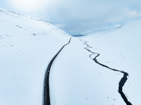 Aerial view of a winding road and a meandering river cutting through a vast snow covered landscape under a bright sky in Egilsstadir Mulathing Iceland. Aerial view of a winding road and a meandering river cutting through a vast snow covered landscape under a bright sky in Egilsstadir Mulathing Iceland.