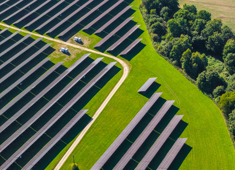 Aerial view of rows of photovoltaic solar panels arranged in a field with a dirt access road and adjacent green forest in Pomeranian Voivodeship Poland. Aerial view of rows of photovoltaic solar panels arranged in a field with a dirt access road and adjacent green forest in Pomeranian Voivodeship Poland.