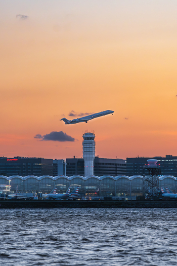 View of Ronald Reagan Washington National Airport with an airplane taking off over the control tower and terminal buildings at sunset in Arlington Virginia United States. View of Ronald Reagan Washington National Airport with an airplane taking off over the control tower and terminal buildings at sunset in Arlington Virginia United States.