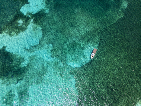 Aerial view of a small boat floating on crystal clear turquoise waters over a coral reef Guanaja Bay Islands Department Honduras. Aerial view of a small boat floating on crystal clear turquoise waters over a coral reef Guanaja Bay Islands Department Honduras.