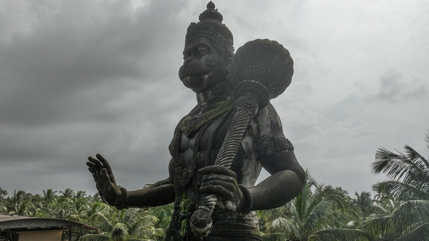 Aerial view of the stone statue of Lord Hanuman holding a mace surrounded by lush palm trees under an overcast sky in Udupi Karnataka India. Aerial view of the stone statue of Lord Hanuman holding a mace surrounded by lush palm trees under an overcast sky in Udupi Karnataka India.