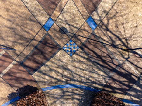 Aerial view of patterned pavement with diamond and square shapes in brown and blue hues overlaid with the stark shadows of bare trees Maastrichtkwartier Flevoland Netherlands. Aerial view of patterned pavement with diamond and square shapes in brown and blue hues overlaid with the stark shadows of bare trees Maastrichtkwartier Flevoland Netherlands.