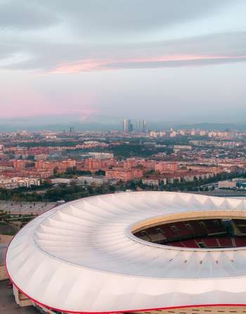 Aerial view of Riyadh Air Metropolitano Stadium with its white roof and red seating set against the urban skyline of Madrid at sunset. Madrid Comunidad de Madrid Spain.
