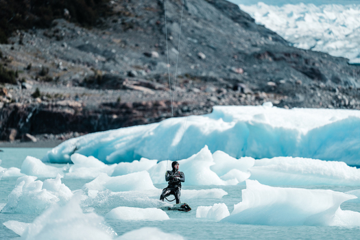 View of a kiteboarder in a wetsuit navigating through floating icebergs in the glacial waters near the Perito Moreno Glacier in Perito Moreno Santa Cruz Province Argentina. View of a kiteboarder in a wetsuit navigating through floating icebergs in the glacial waters near the Perito Moreno Glacier in Perito Moreno Santa Cruz Province Argentina.