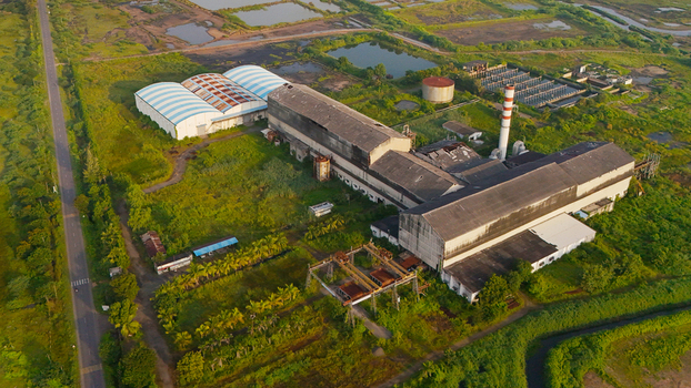 Aerial view of an industrial factory complex with a large warehouse a tall chimney and surrounding green fields and water ponds in Olpad Gujarat India. Aerial view of an industrial factory complex with a large warehouse a tall chimney and surrounding green fields and water ponds in Olpad Gujarat India.
