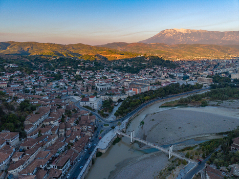 Aerial view of historic Berat featuring traditional Ottoman style houses the Osum River and a pedestrian bridge set against mountains in Berat Berat County Albania.