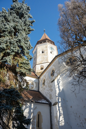 View of the historic Prejmer Fortified Church featuring a tall clock tower white stone walls and a tiled roof under a clear blue sky in Prejmer Brasov Romania. View of the historic Prejmer Fortified Church featuring a tall clock tower white stone walls and a tiled roof under a clear blue sky in Prejmer Brasov Romania.