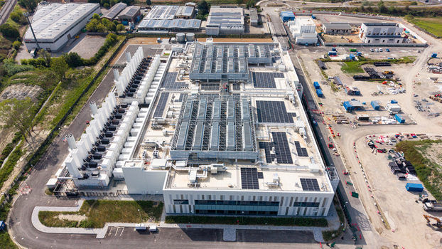 Aerial view of a modern hyperscale data center featuring extensive rooftop solar arrays industrial cooling systems and surrounding infrastructure in Melegnano Lombardy Italy.