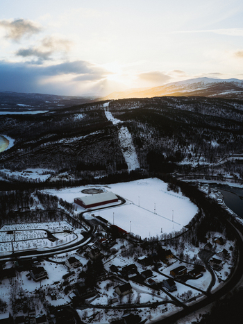 Aerial view of snow covered fields meet dark forests under a sky streaked with golden sunset hues casting long shadows over the landscape Sjøvegan Troms Norway. Aerial view of snow covered fields meet dark forests under a sky streaked with golden sunset hues casting long shadows over the landscape Sjøvegan Troms Norway.