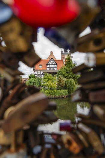 View of a historic half timbered building with a red roof reflected in the canal framed by blurred love padlocks on a bridge in Gdansk Pomeranian Voivodeship Poland. View of a historic half timbered building with a red roof reflected in the canal framed by blurred love padlocks on a bridge in Gdansk Pomeranian Voivodeship Poland.