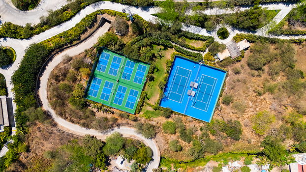 Aerial view of tennis courts nestled amidst winding paths and verdant foliage creating a vibrant contrast of blues and greens Riviera Nayarit Mexico