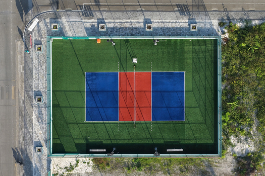 Aerial view of a fenced sports court with a green artificial turf surface and a blue and red central playing area in Kudahuvadhoo Dhaalu Atoll Maldives.