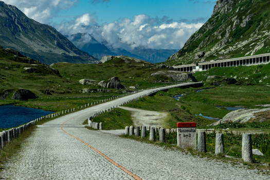 View of the historic Tremola cobblestone road winding through the rugged alpine landscape of the Sankt Gotthard Pass with green slopes and peaks Airolo Ticino Switzerland.