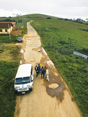 Aerial view of a weathered road snaking through vibrant emerald hills a white van and people paused on its rugged surface Obudu Cross River Nigeria.