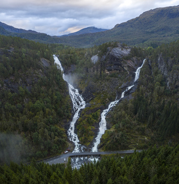 Aerial view of the twin waterfalls of Latefossen cascading down rocky cliffs surrounded by dense green pine forests under a cloudy sky Skare Vestland Norway.
