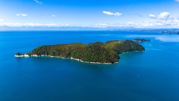 Aerial view of an island with lush green vegetation surrounded by the deep blue sea Abel Tasman National Park Tasman Region New Zealand. Aerial view of an island with lush green vegetation surrounded by the deep blue sea Abel Tasman National Park Tasman Region New Zealand.