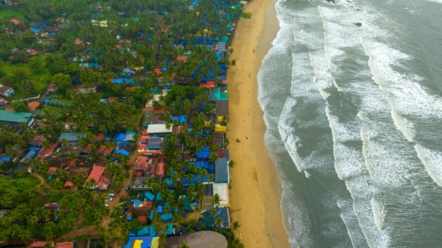 Aerial view of Palolem Beach with golden sands turquoise waves and dense palm trees featuring colorful beach huts nestled among the greenery in Canacona Goa India.