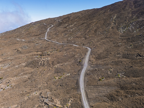 Aerial view of the winding road on the slopes of Mauna Kea volcano with barren volcanic terrain and clear blue sky Hawaii County Hawaii United States.
